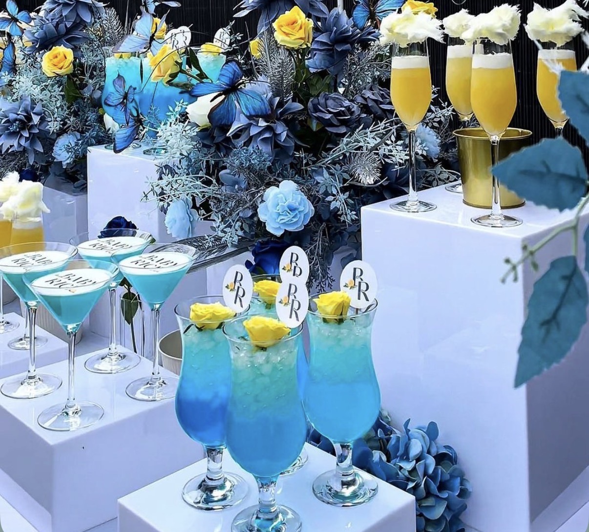 Blue signature cocktails and mimosas on white pedestals with florals